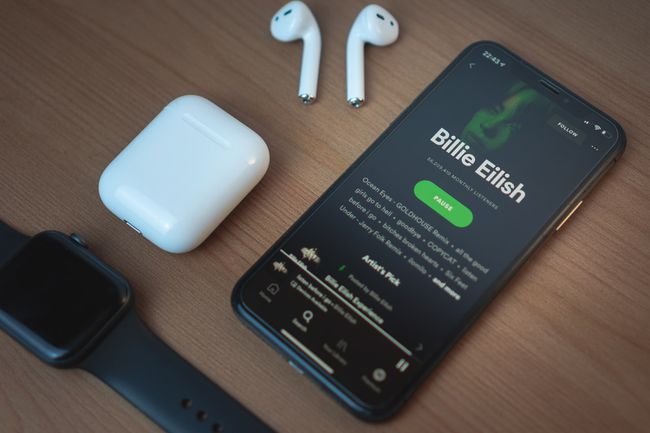 アップルウォッチとAirPodsの横にある木製のテーブルにSpotifyを表示している黒いiPhone