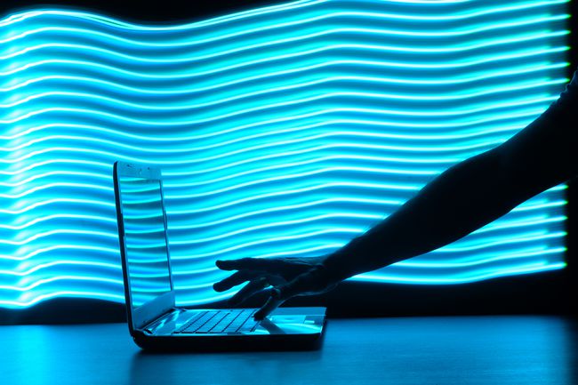 Neon mavisi, dalgalı arka planı olan bir dizüstü bilgisayarda birinin elinin silueti. 