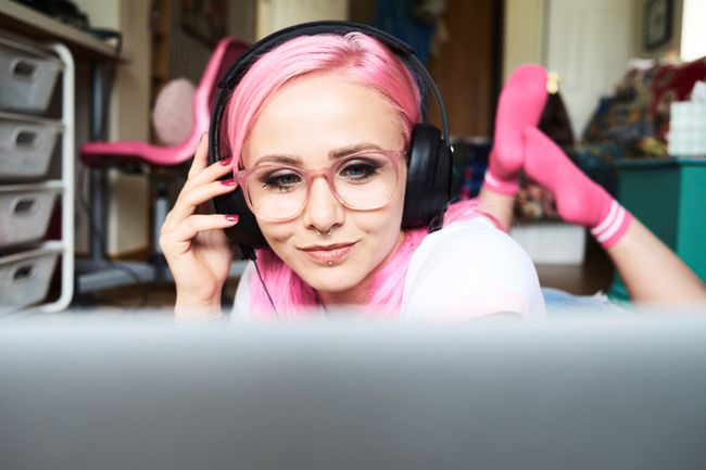 Pembe saçlı genç kadın evde dizüstü bilgisayardan müzik dinliyor.