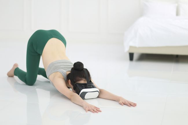 En person, der laver yoga på et hvidt gulv i et hvidt rum, mens han bærer et virtual reality-headset.