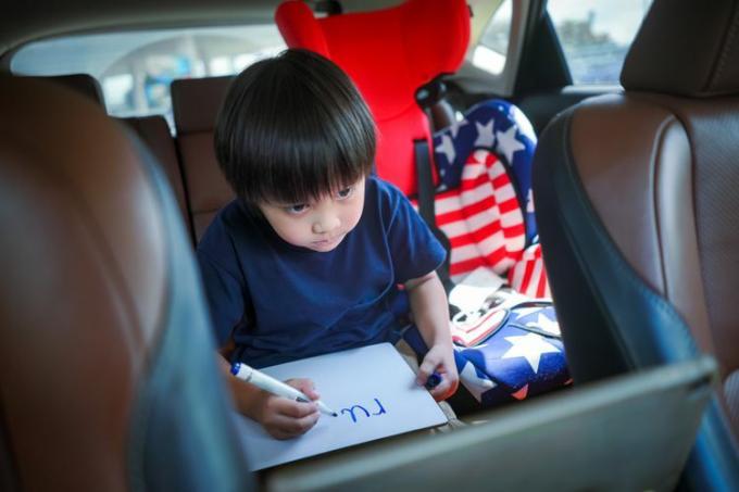 Niño pequeño que estudia en línea con una tableta en el asiento trasero de un automóvil