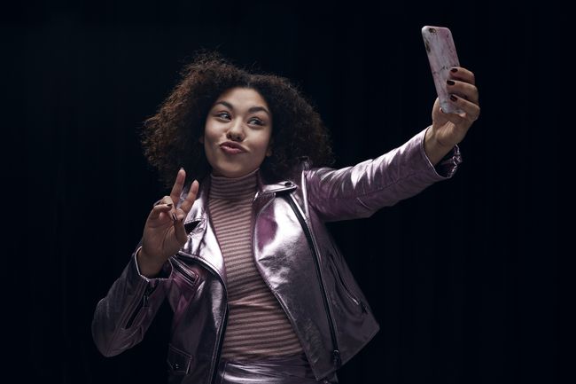 Rauhanmerkkiä tekevä nainen ottaa selfietä.