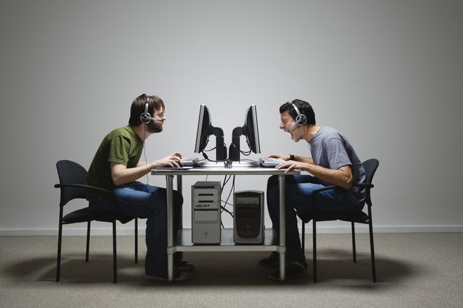 Profil dwóch mężczyzn korzystających z komputerów siedzących naprzeciwko siebie przy biurku