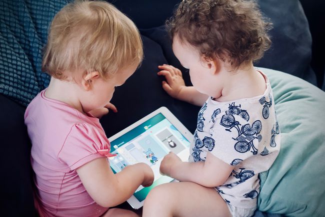 to småbørn, der sidder i en sofa og bruger en iPad