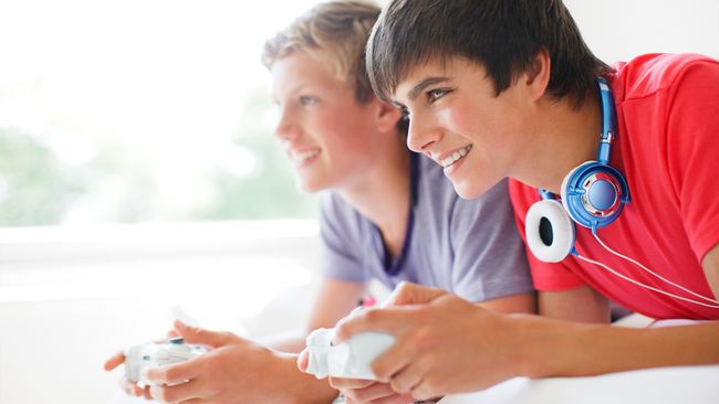 To tenåringsgutter spiller Xbox-videospill mens de ligger på en seng