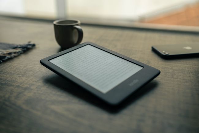 Електронен четец на Kindle, стоящ на плота с чаша кафе и iphone наблизо.