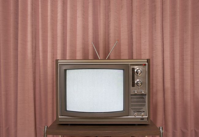 Старый телевизор на подставке перед занавеской