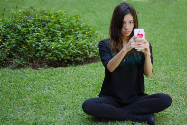 Uma pessoa sentada na grama usando um telefone celular