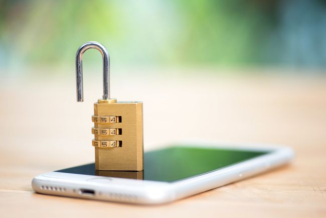 Um cadeado de combinação aberto em cima de um smartphone que está sobre a mesa.