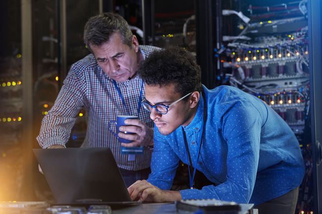 Técnicos de TI masculinos concentrados que trabajan en la computadora portátil en la sala de servidores oscura