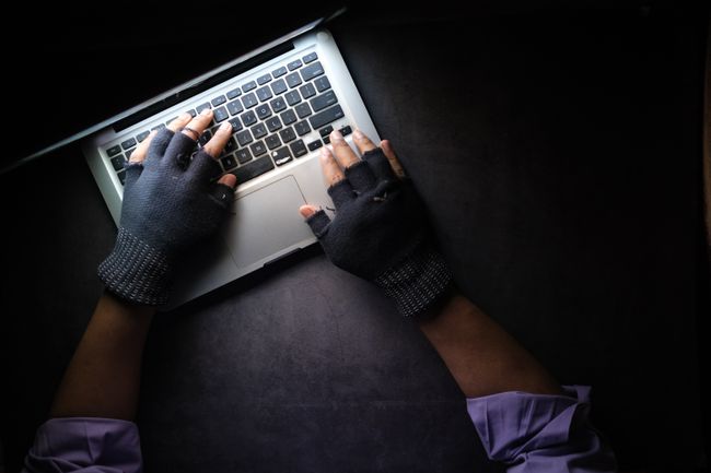 Mâinile unui hacker pe tastatura unui laptop, iluminate de ecranul computerului.
