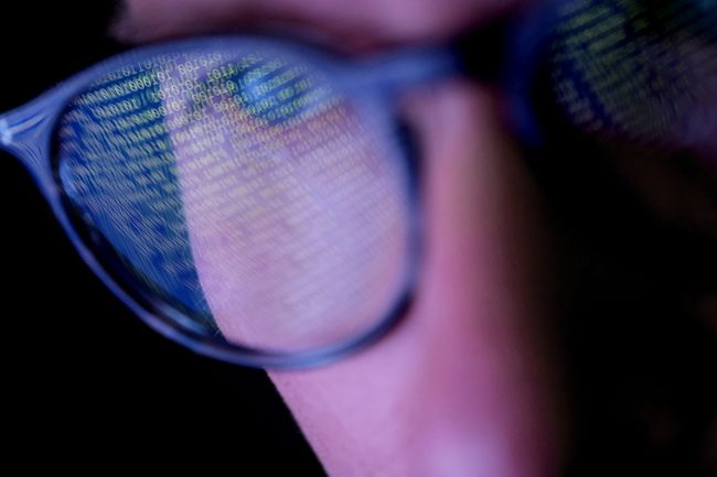 Et nærbillede af en person, der bærer briller med binær kode, der reflekterer på linserne. 