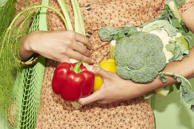 新鮮な野菜の腕一杯を保持している誰かのクローズアップ。