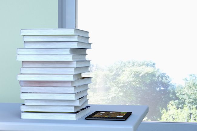 E-Reader und Bücherstapel auf einem Tisch vor einem Fenster liegend, 3D-Rendering