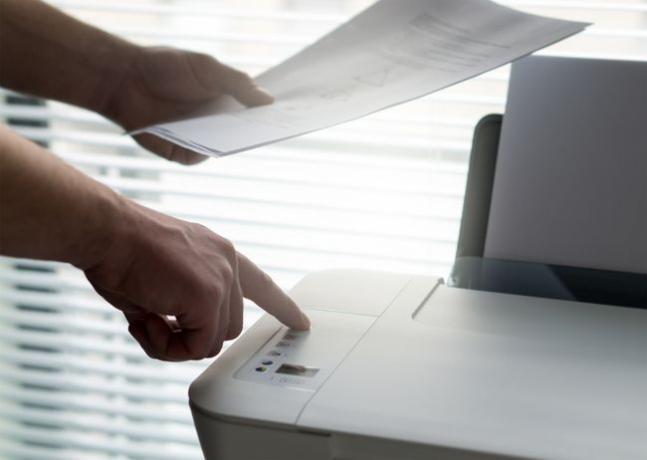 종이를 들고 프린터의 버튼을 눌러 인쇄 작업을 중지하는 사람
