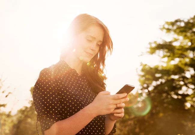 後ろに明るい太陽が降り注ぐスマートフォンを使用している人。