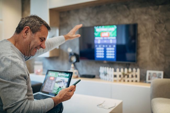 Volwassen man die mobiele app gebruikt voor live wedden en online gokken en naar een sportwedstrijd kijkt
