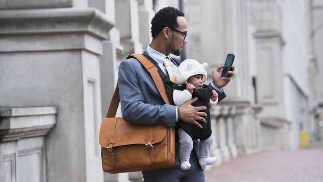 Uomo d'affari con figlio nel marsupio che manda messaggi al cellulare