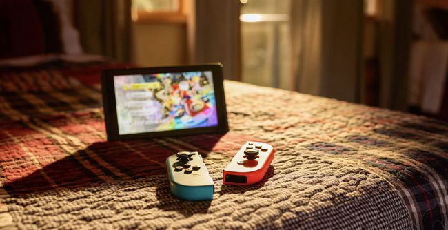 Nintendo Switch พร้อมขาตั้งและตัวควบคุม Joy-Con วางอยู่บนเตียง