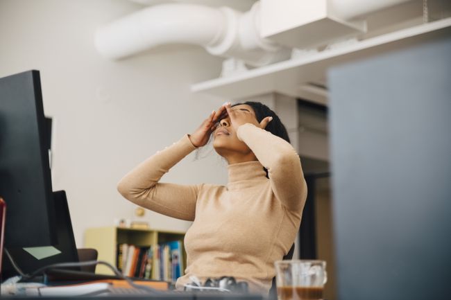 한 여성이 컴퓨터 앞에 앉아 있지만 좌절감에 눈을 비비며 등을 기대고 있습니다.