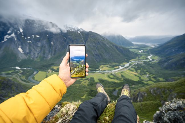 iPhoneで写真を撮る巨大な谷の頂上に座っている男