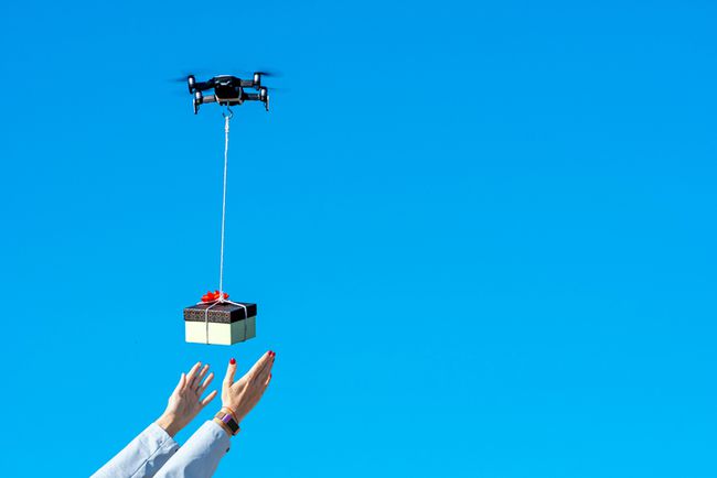 青空に対してドローンによって運ばれる贈り物のために手を差し伸べる人