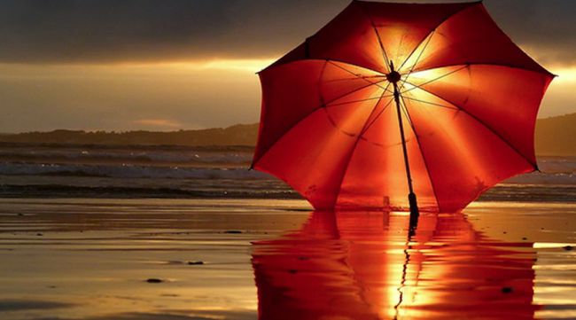 Fondo de pantalla de playa gratuito con una sombrilla roja al atardecer