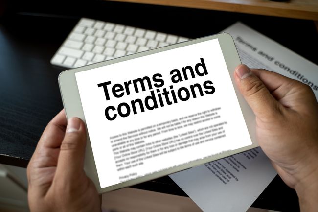 En person, der bruger en tablet til at læse " Vilkår og betingelser" med et papirdokument og et tastatur i baggrunden.